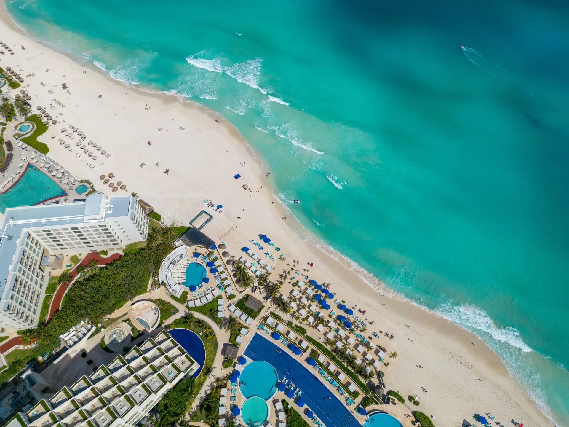 Overhead aerial view of a Cancun beachfront resort with curving pools and turquoise water, Mexico